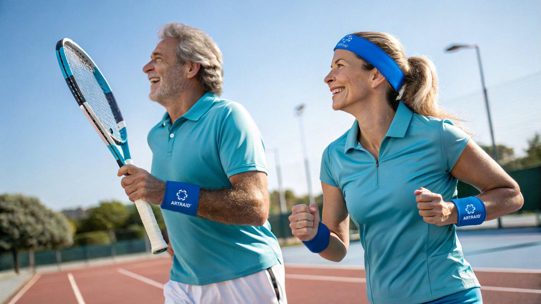 Aktyvi pora teniso aikštelėje su ARTRAID sportinėmis riešinėmis ir galvos juosta, besimėgaujanti sportu ir judėjimu lauke.
